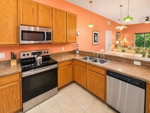 A kitchen with wooden cabinets, stainless steel appliances, a dishwasher, and a dining area with a sofa and table.