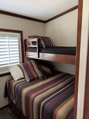 A bunk bed with a striped bedspread and pillows, a wooden headboard, and a window with blinds. - Ben Ranch Cabin #1 . Located in century old Pecan Orchard, historic Osage County (Ralston)