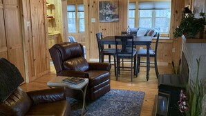 A cozy cabin interior with a leather sofa, a dining table, and a fireplace.