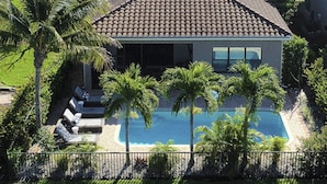 Un barrio residencial con una casa de techo de tejas, piscina y palmeras.