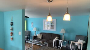 Sala de estar com parede azul, sofá marrom, duas poltronas, mesa de centro e duas luminárias pendentes.