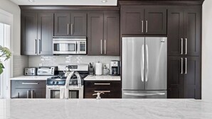 Cozinha moderna com armários escuros, eletrodomésticos de aço inoxidável e bancada de mármore.