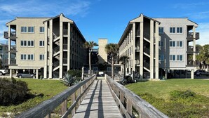 Un immeuble d’appartements moderne doté d’une entrée centrale, de nombreux balcons et d’une passerelle en bois menant à l’entrée.