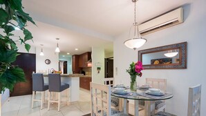 Un comedor con una mesa de vidrio, sillas con cojines estampados, un florero con flores y un espejo montado en la pared.