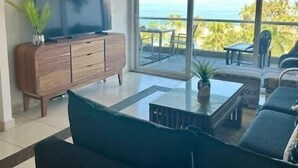 Una sala de estar con televisor, sofá, mesa de centro y un balcón con vista al océano.