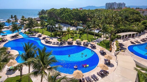 Un resort con varias piscinas, palmeras y vista al océano.