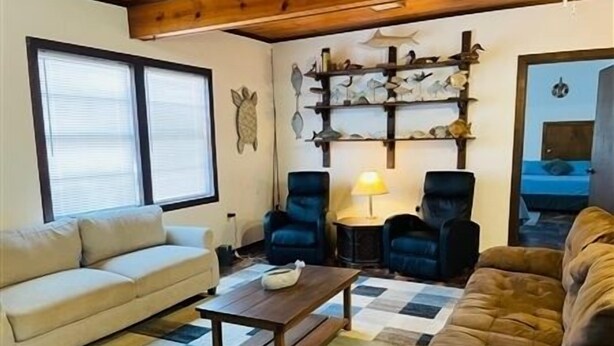 Una sala de estar con un sofá color beige, un sofá marrón y dos sillones azules. Hay una mesa de centro de madera y una lámpara sobre una mesita auxiliar. Se observa una obra de arte mural con motivos de peces.