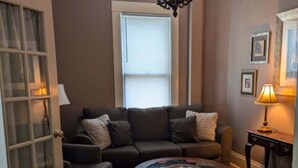 A living room with a brown sofa, a round coffee table, and a chandelier. - The Gate House (Entire House) (Lancaster)