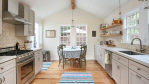 A kitchen with a central island, wooden cabinets, a stove, and a large window. - Baytree Cottage | Beautiful Stay w/ Amazing Views (Inverness)