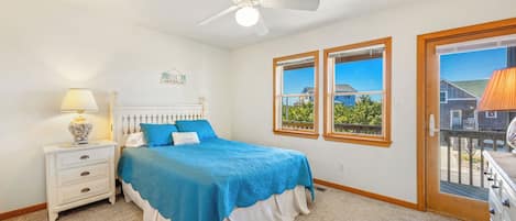 Un dormitorio con cama, mesita de noche, lámpara, ventilador de techo y ventana con vistas.