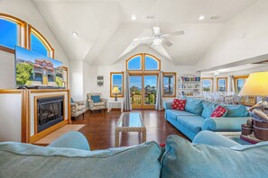 A spacious living room with a fireplace, a large sofa, a coffee table, and a view of the outside through large windows.