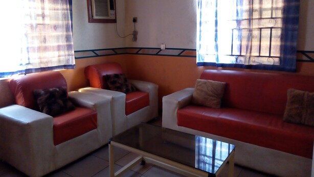 A living room with two red sofas, a glass coffee table, and a wall-mounted air conditioner. - Adebayowa Hotel (Lagos)