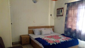 A bedroom with a bed, nightstand, and a small window with curtains. - Adebayowa Hotel (Lagos)