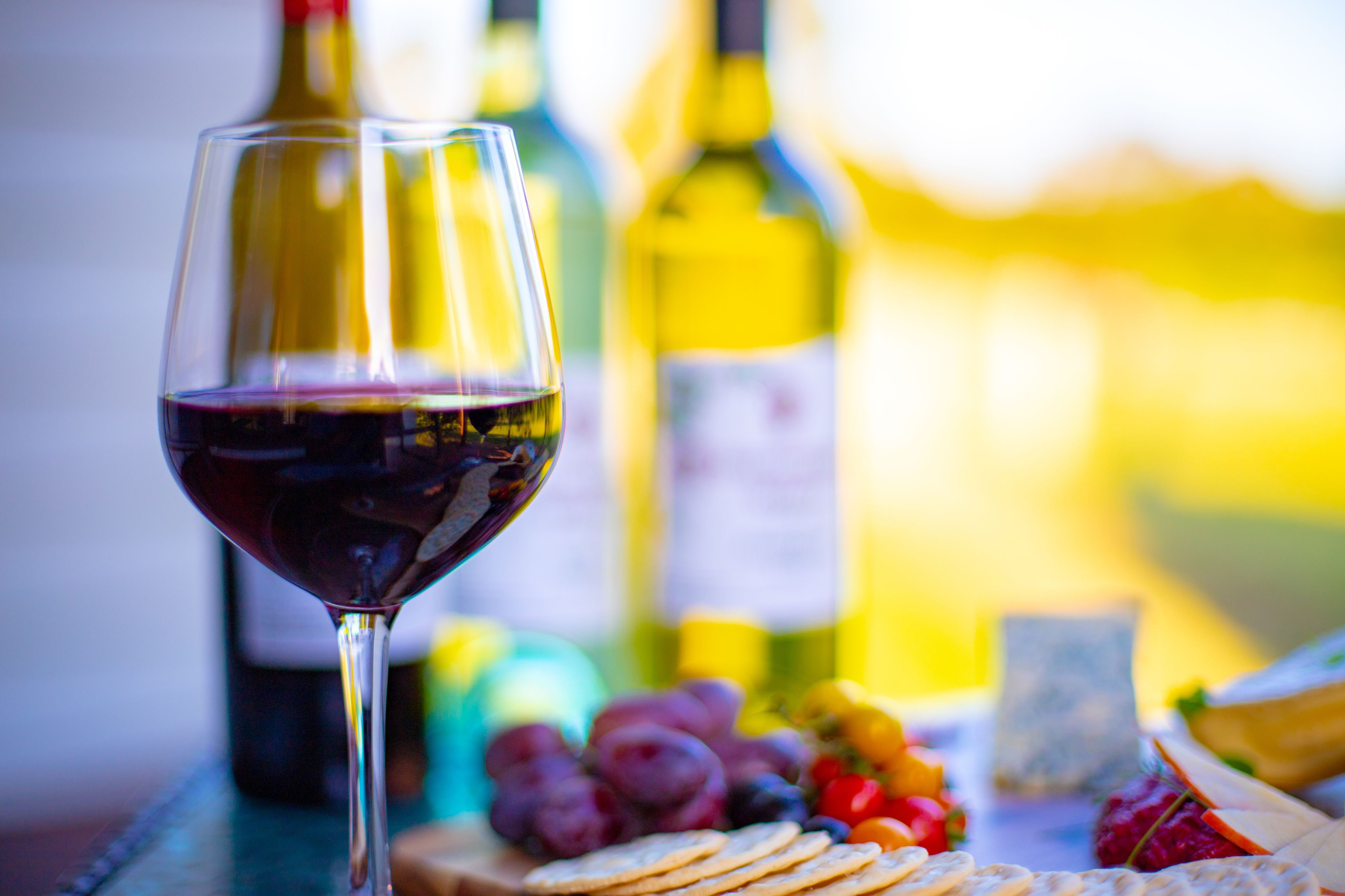 A wine glass with red wine, a bottle of wine, and a variety of fruits and cheeses on a table.