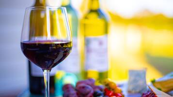 A wine glass with red wine, a bottle of wine, and a variety of fruits and cheeses on a table.