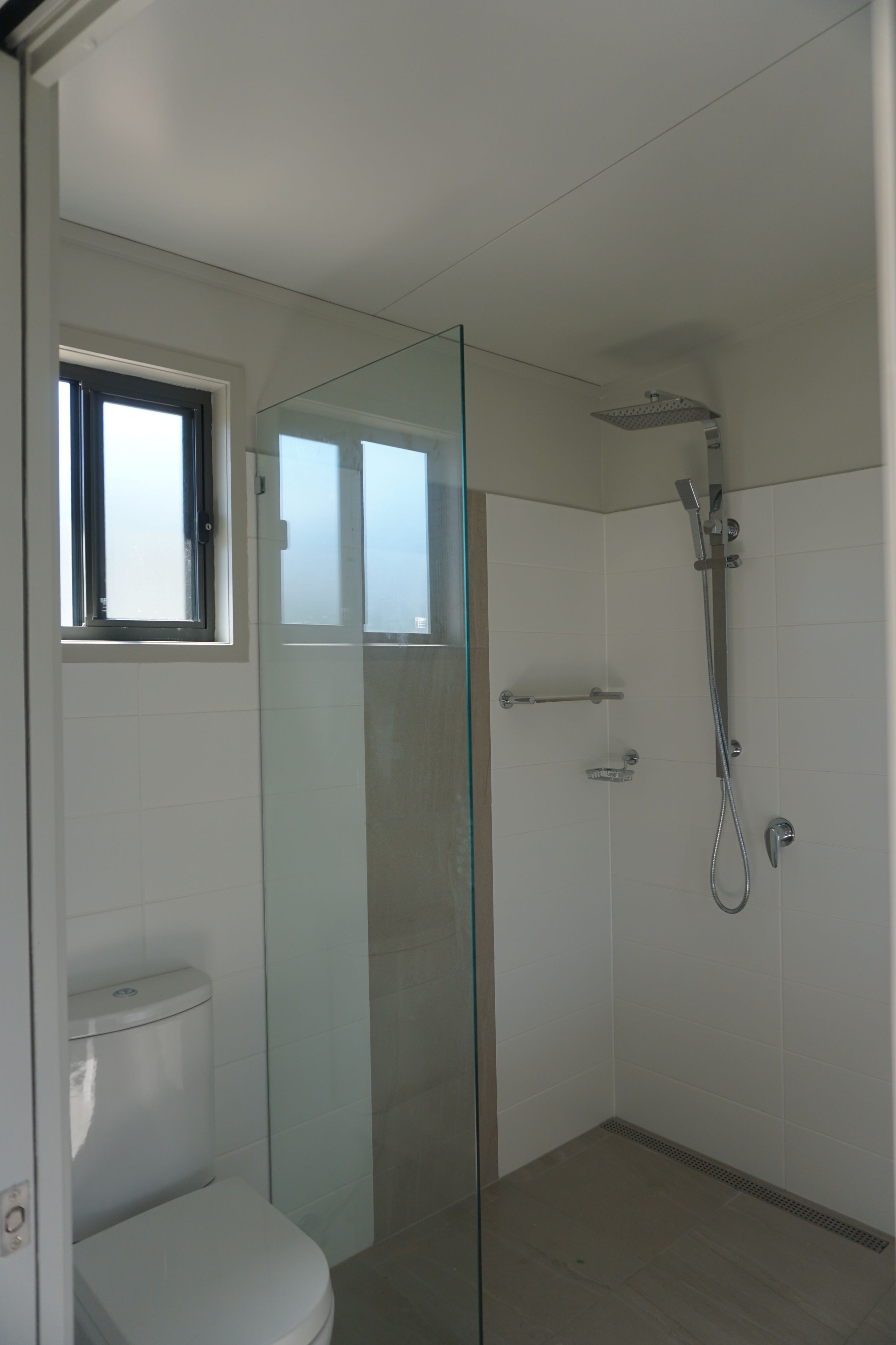 A bathroom with a glass-enclosed shower, a toilet, and a window.