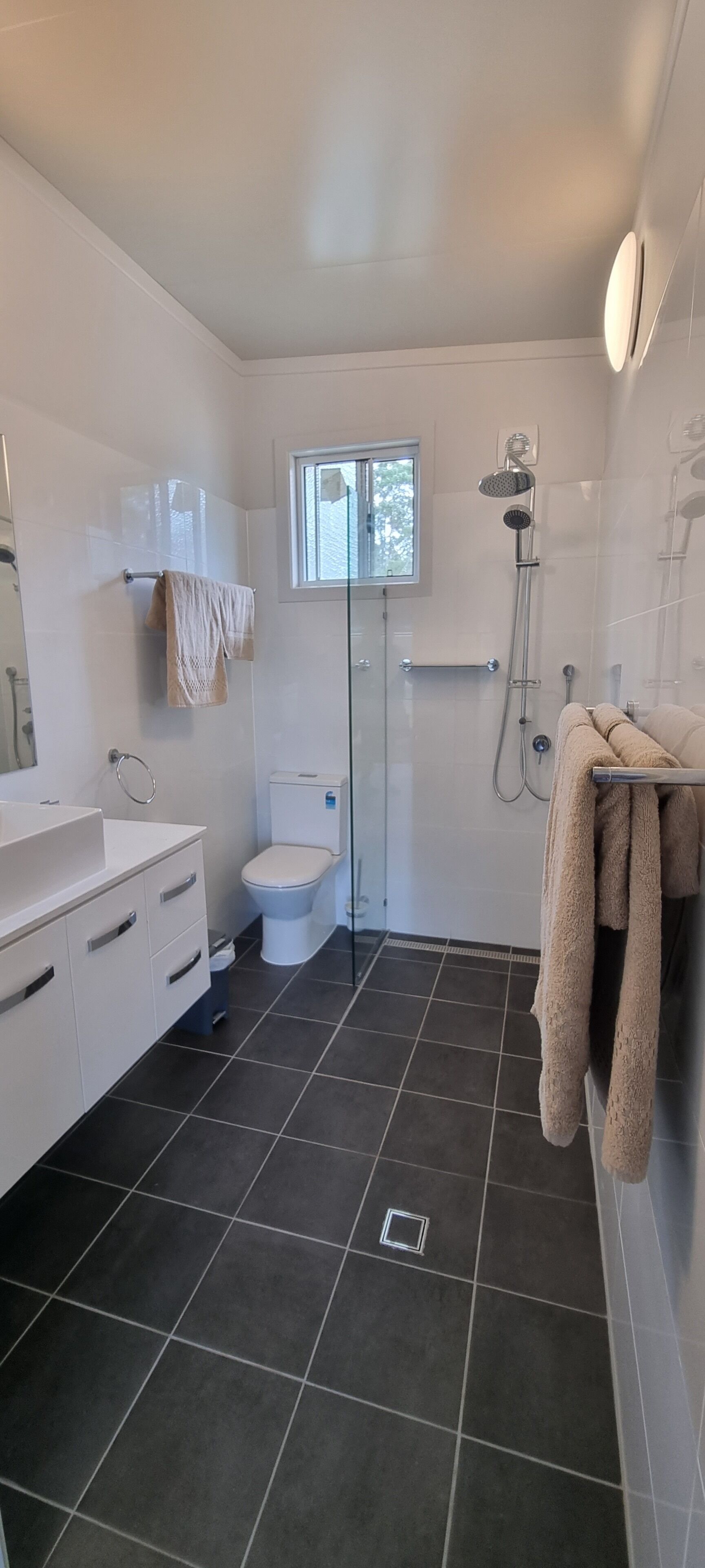 Un baño moderno con lavamanos, inodoro y zona de ducha blancos.
