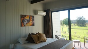 Une chambre avec un grand lit, un tableau accroché au mur et une vue sur un espace verdoyant par la fenêtre.