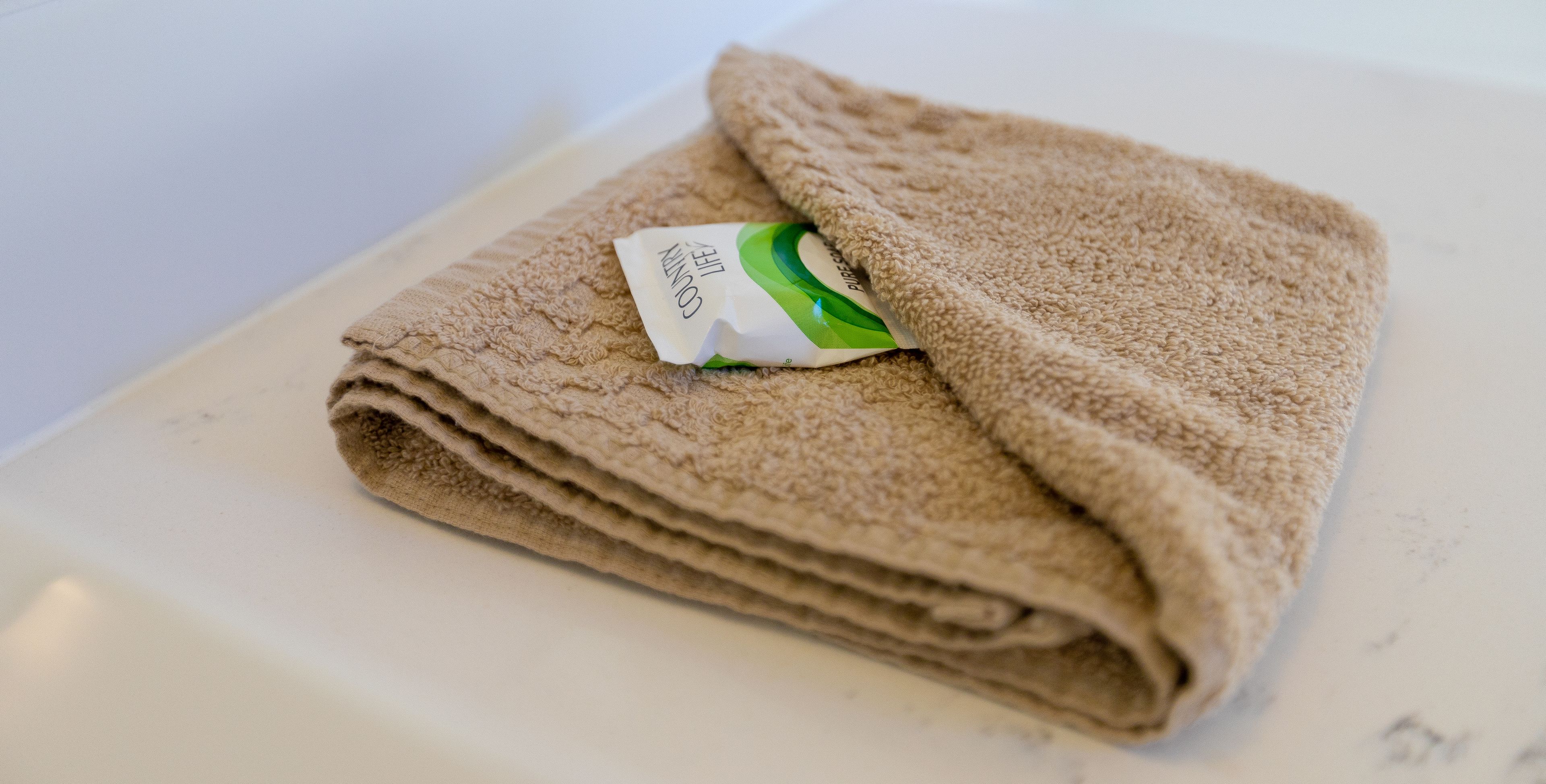 A folded beige towel with a tag on a white surface.