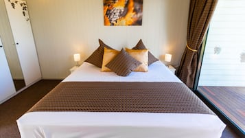 A neatly made bed with a patterned bedspread and pillows, a wall-mounted artwork, and a window with curtains.