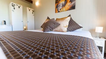 Una cama bien hecha con una colcha estampada, una mesita de noche con una lámpara y una obra de arte colgada en la pared.