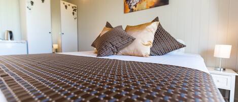 A neatly made bed with a patterned bedspread, a bedside table with a lamp, and a wall-mounted artwork.