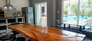 Una cocina con una mesa de madera, sillas, un refrigerador y vistas a una piscina.