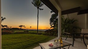 Eine Terrasse mit Tisch für zwei Personen, mit Blick auf einen Sonnenuntergang, Palmen und eine Rasenfläche.