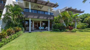 Ein modernes, zweistöckiges Haus mit überdachter Veranda, Palmen und einem gepflegten Rasen.