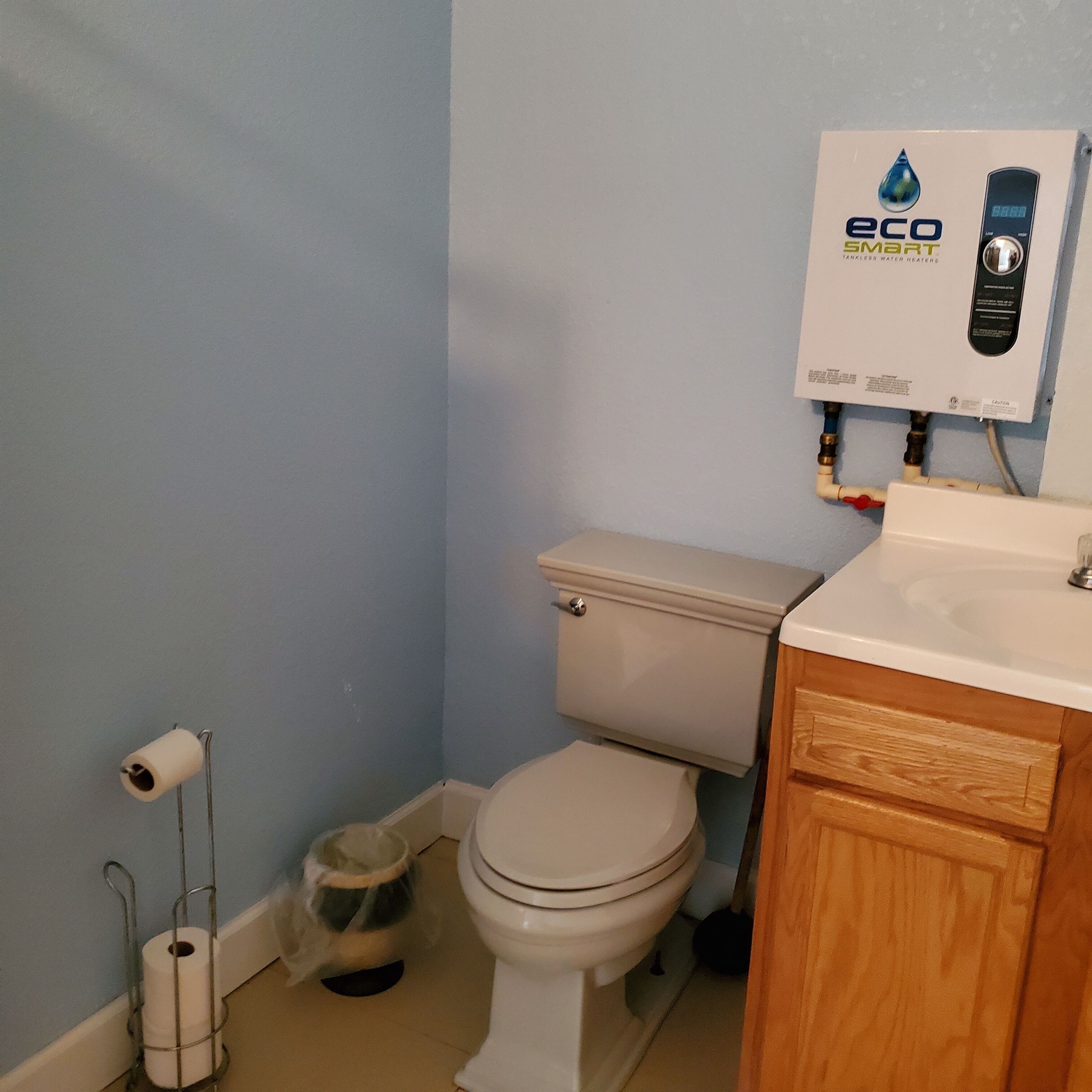 A bathroom with a toilet, a white sink, and an eco smart water heater.