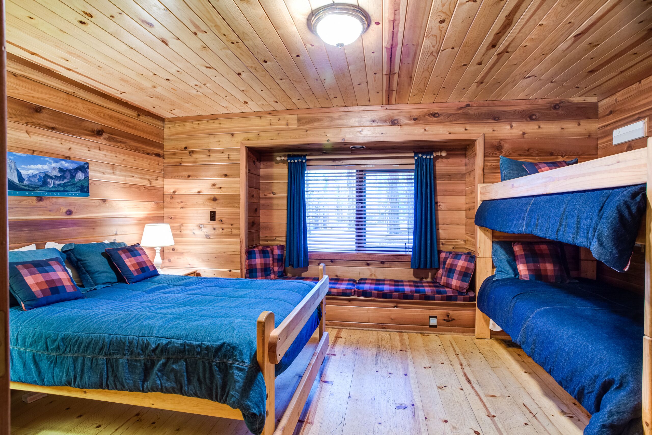 Een houten kamer met een stapelbed, een enkel bed en een raam met gordijnen.