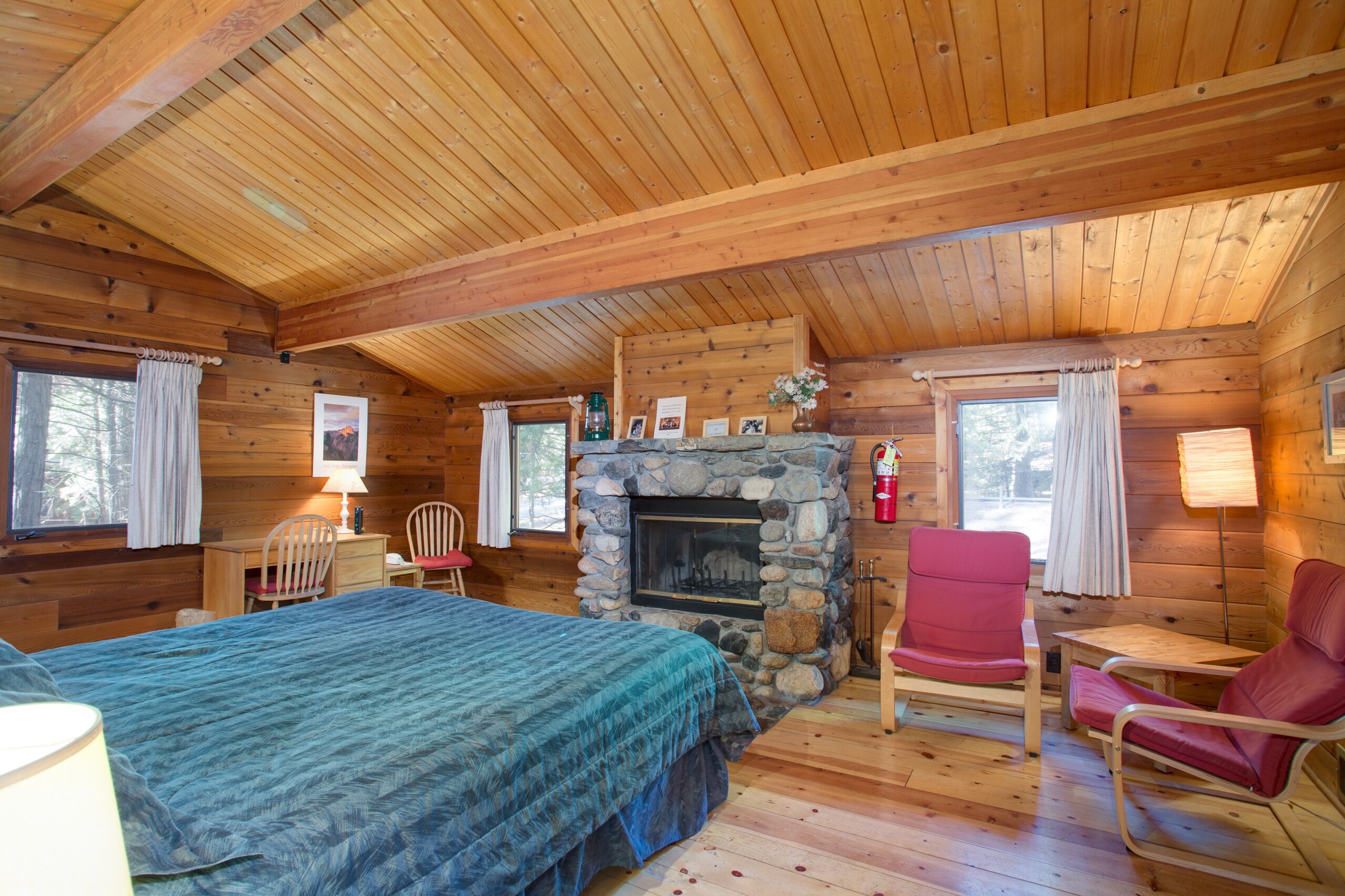 Une chambre rustique en rondins de bois, avec un lit, une cheminée en pierre, une table à manger et une chaise rouge.