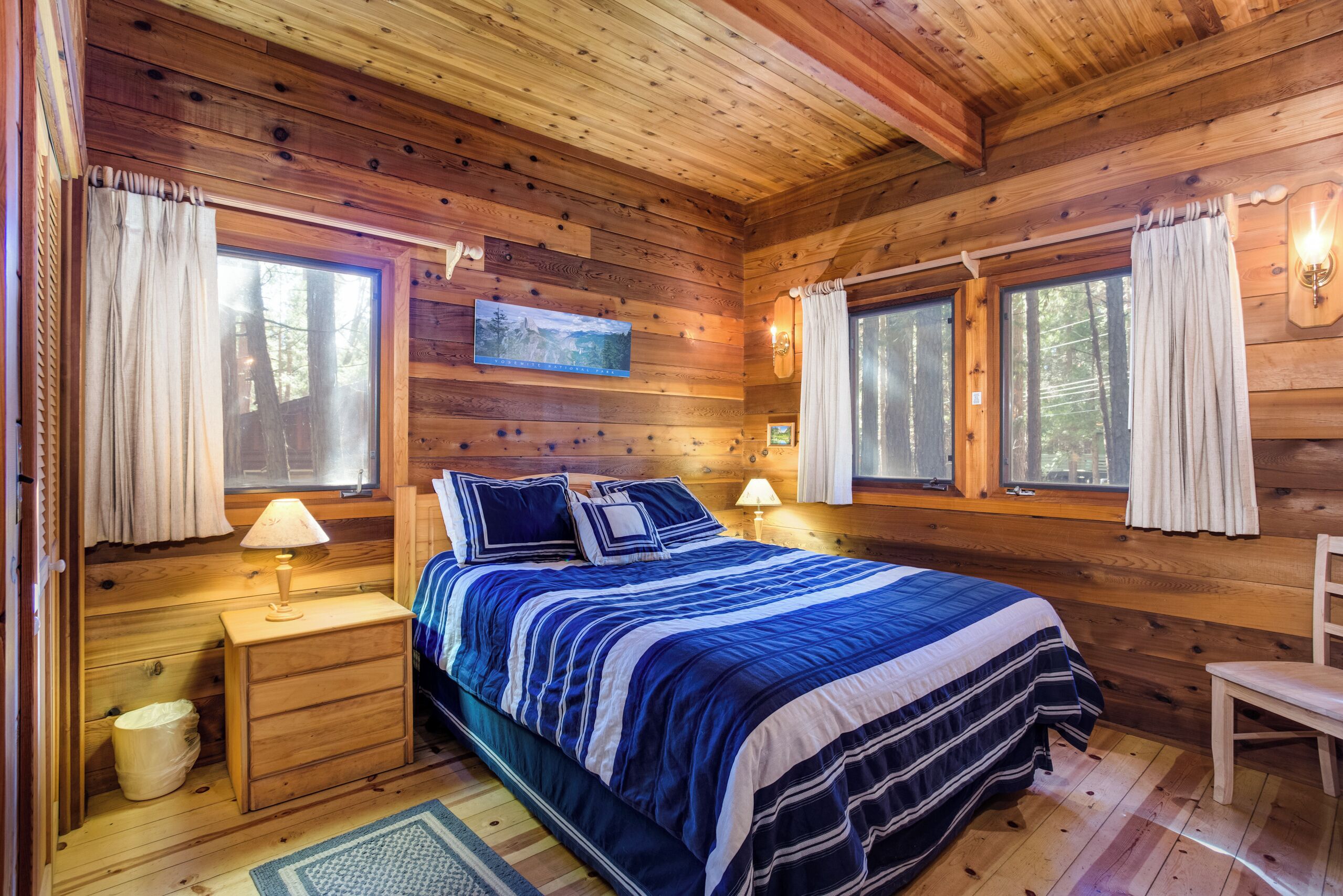 A wooden cabin bedroom with a bed, bedside tables, and windows.