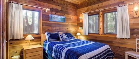 A wooden cabin bedroom with a bed, bedside tables, and windows.