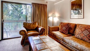 A living room with a leather sofa, a patterned coffee table, a floor lamp, and a large window with curtains.