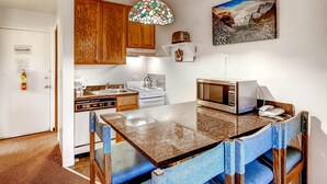 A kitchen with wooden cabinets, a granite countertop, a microwave, a stove, and a hanging light fixture.