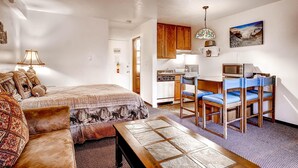 A cozy room with a bed, a wooden table, and a kitchenette.