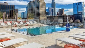 A rooftop pool with lounge chairs, a diving board, and a city skyline in the background. - Austin | Couples ATX Base | Pool + Gym (Austin)