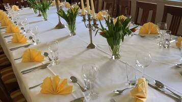 A long dining table set with white tablecloths, yellow napkins, and candle holders.