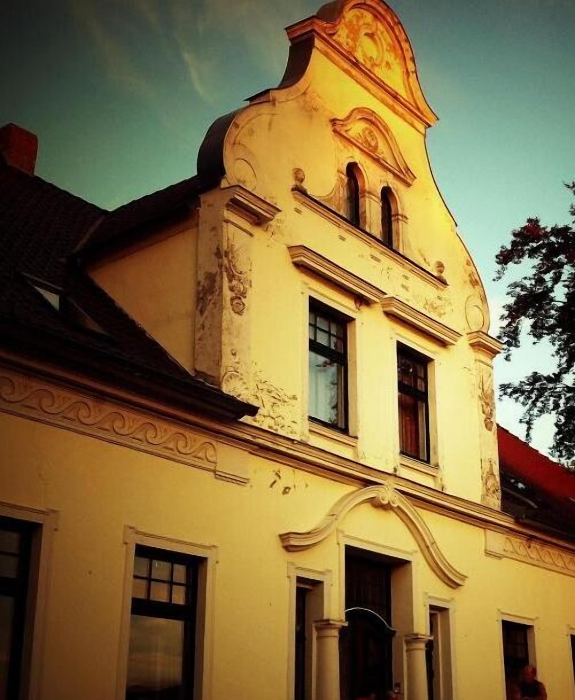 A building with a classical architectural style, featuring a prominent central section with a pediment and a smaller section with a balcony.