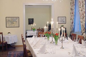 Uma sala de jantar com uma mesa comprida posta para refeição, com castiçais e centros de mesa florais.