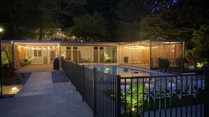Un área de piscina moderna al aire libre, con una zona de estar cubierta, un sendero y una valla.