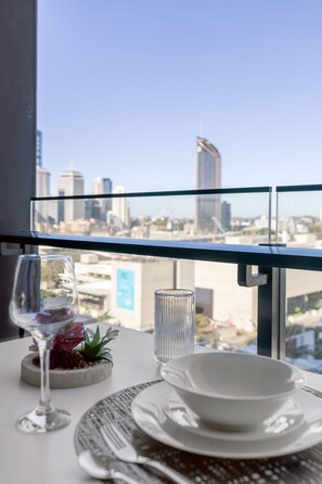 Una mesa de comedor con una copa de vino, un bol y una vela, con vistas a un paisaje urbano con edificios altos.