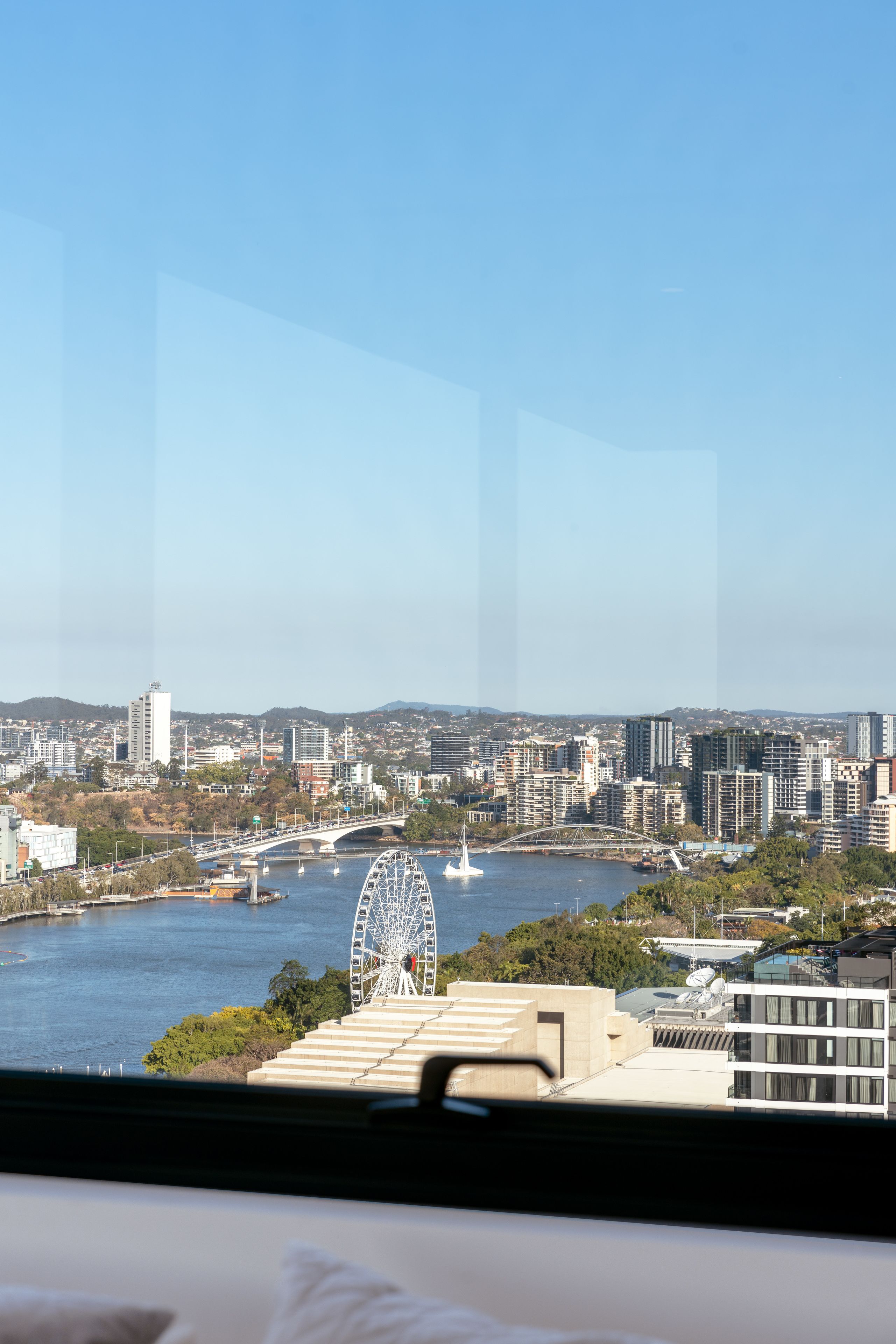 Une vue urbaine comprenant une grande roue, un pont et une étendue d’eau.