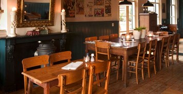 Um restaurante acolhedor com mesas e cadeiras de madeira, uma lareira e um espelho na parede.