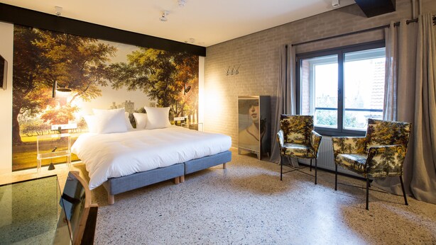 Ein modernes Schlafzimmer mit einem großen Bett, einer Sitzecke mit Stühlen, einem großen Fenster mit Vorhängen und einem Wandgemälde mit Stadtansicht.