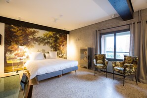 A modern bedroom with a large bed, a seating area with chairs, a large window with curtains, and a cityscape mural on the wall. - Designhotel Napoleonschuur (Amerongen)