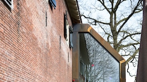 Ein Backsteinhaus mit moderner Glaseingang und einem Kiesweg, der davor führt.