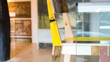 A chair with a wooden backrest and a glass seat in a room with a concrete floor and a cabinet with artwork.