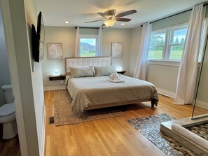 Relax in this serene bedroom with a large bed, tufted headboard, and plush pillows, surrounded by a beautiful view.